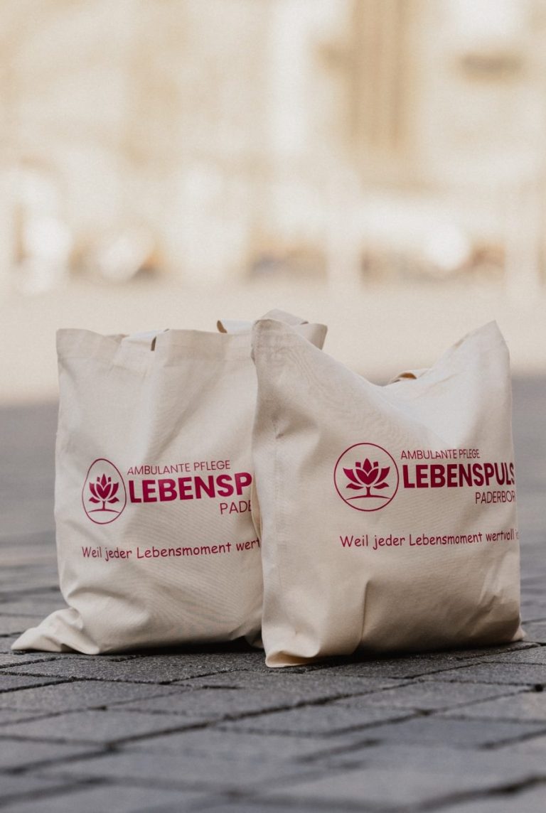 Zwei Stoffbeutel mit dem Aufdruck "LEBENSPULS Paderborn" in einem urbanen Umfeld.